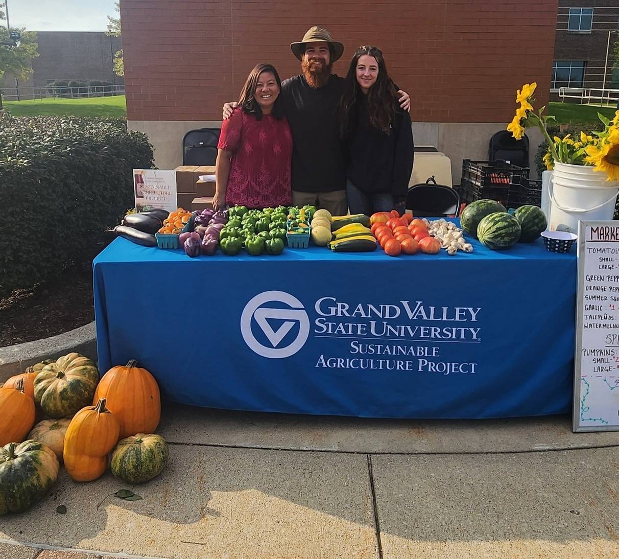 three people standing behind a table with fall produce for sale